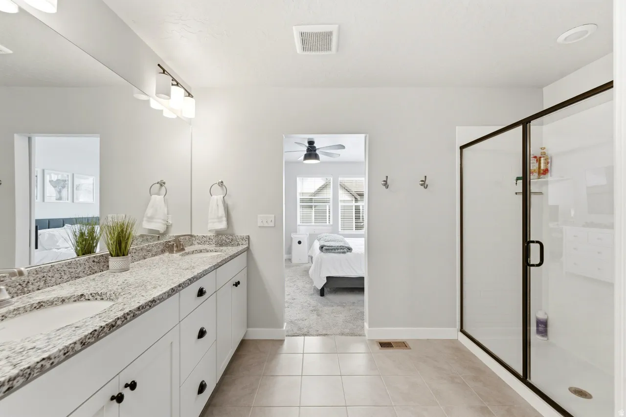 Bathroom featuring connected bathroom, a stall shower, double vanity, and light tile patterned floors