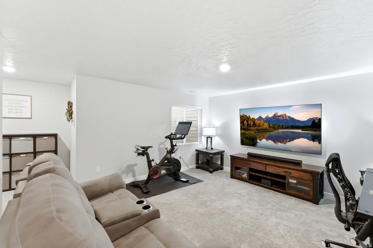 Living area with light colored carpet, a desk, and a textured ceiling