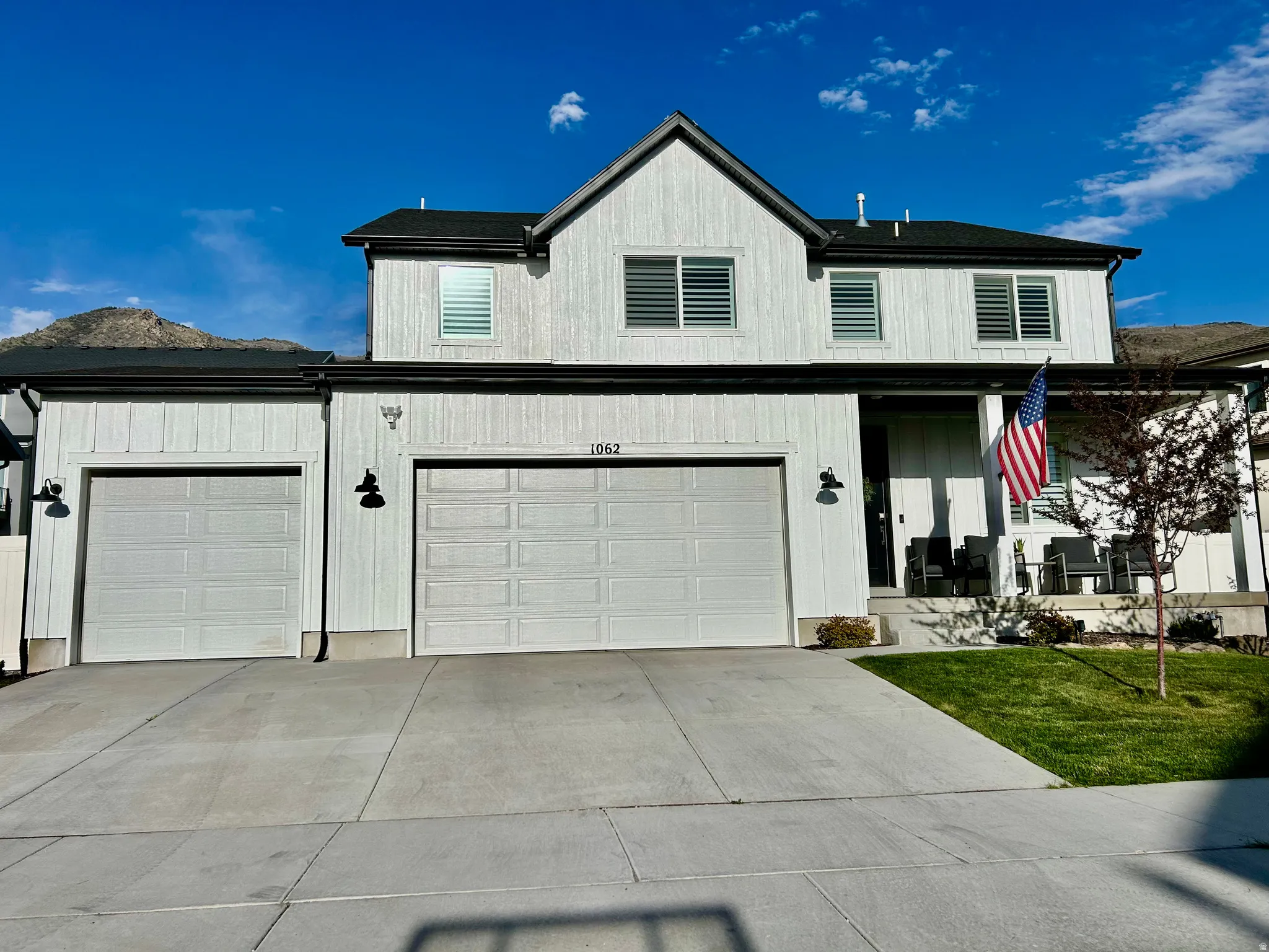 Modern inspired farmhouse featuring a porch, driveway, and a 3 car garage, with mountains behind