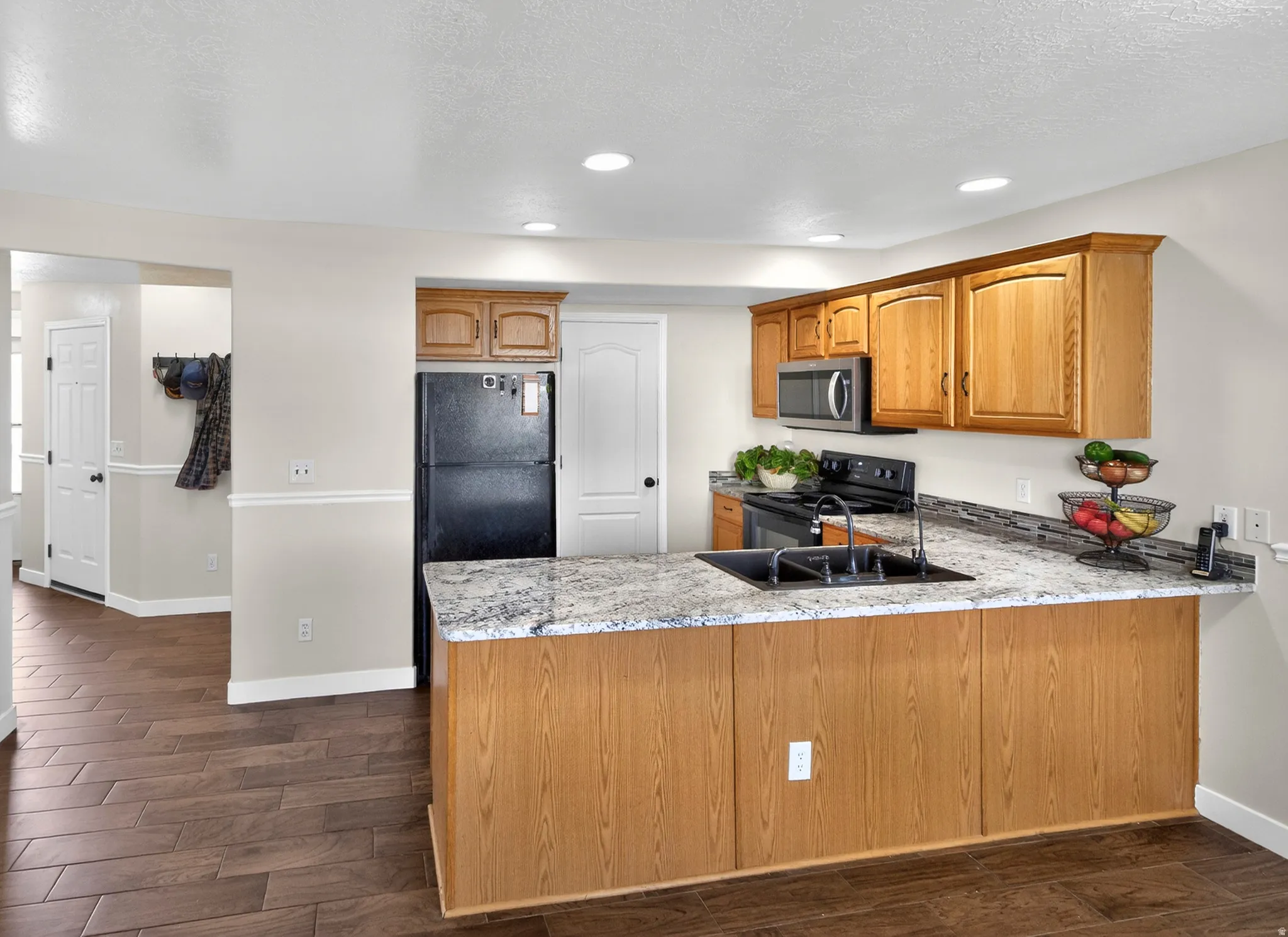 Kitchen featuring dark wood finished floors, black appliances, a peninsula, wood finish cabinetry, and recessed lighting