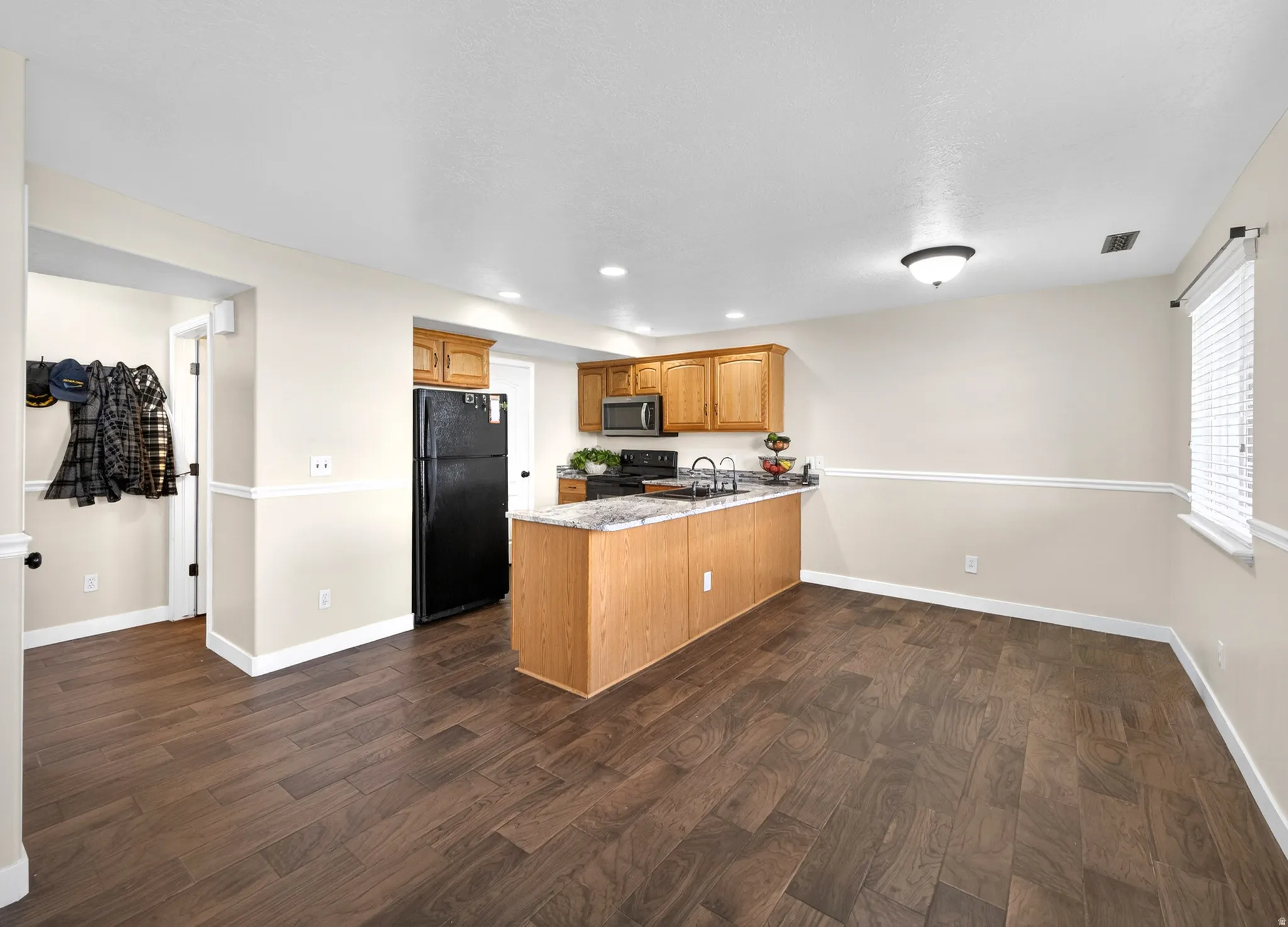 Kitchen featuring a peninsula, dark wood-type flooring, black appliances, recessed lighting, and light stone countertops
