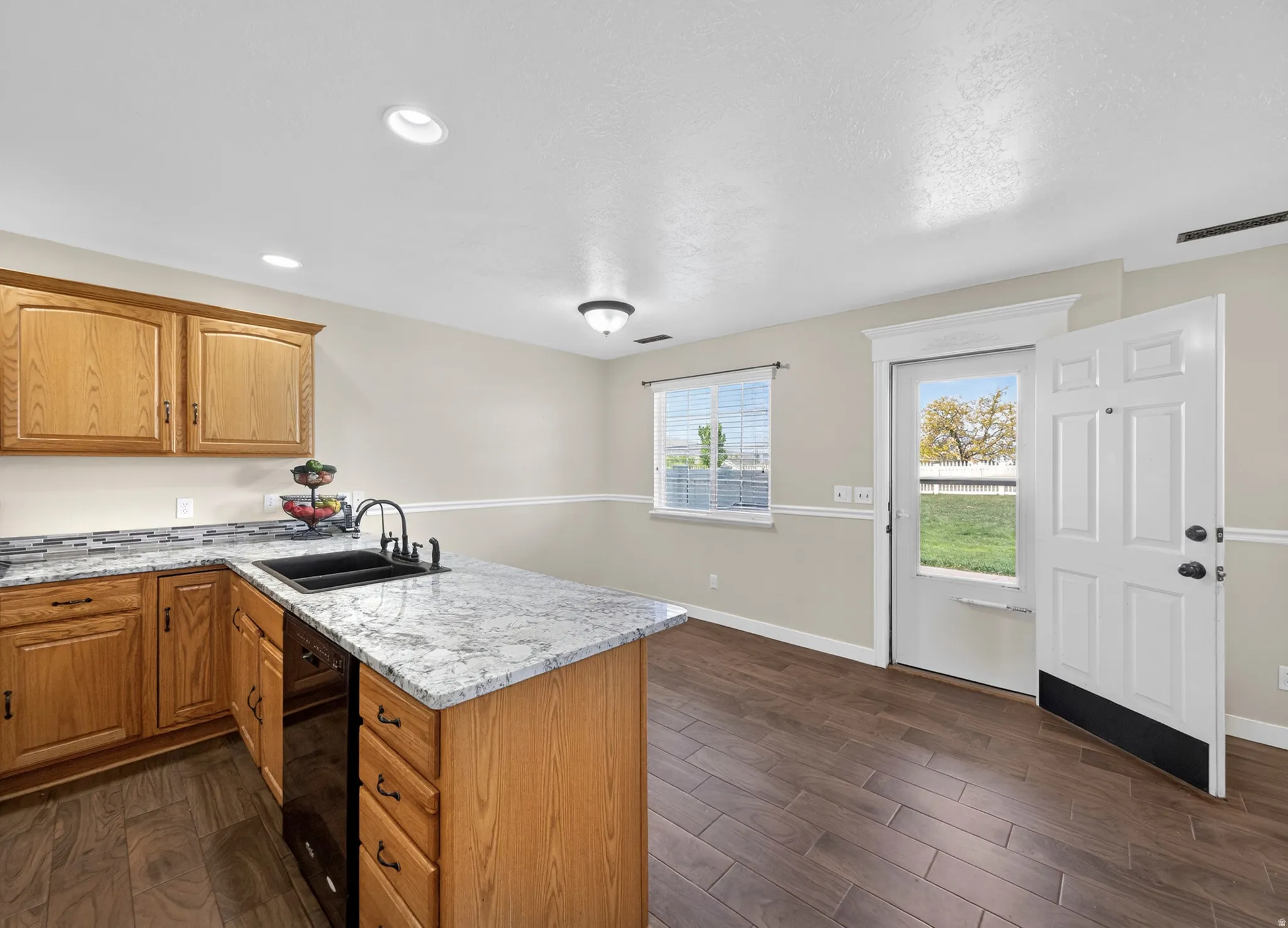 Kitchen with a peninsula, dark wood-style floors, light stone countertops, dishwasher, and wood finish cabinets