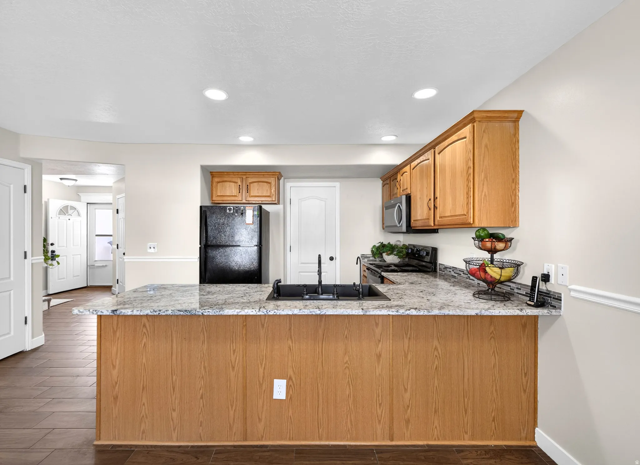 Kitchen with a peninsula, dark wood-type flooring, black appliances, wood finish cabinetry, and recessed lighting