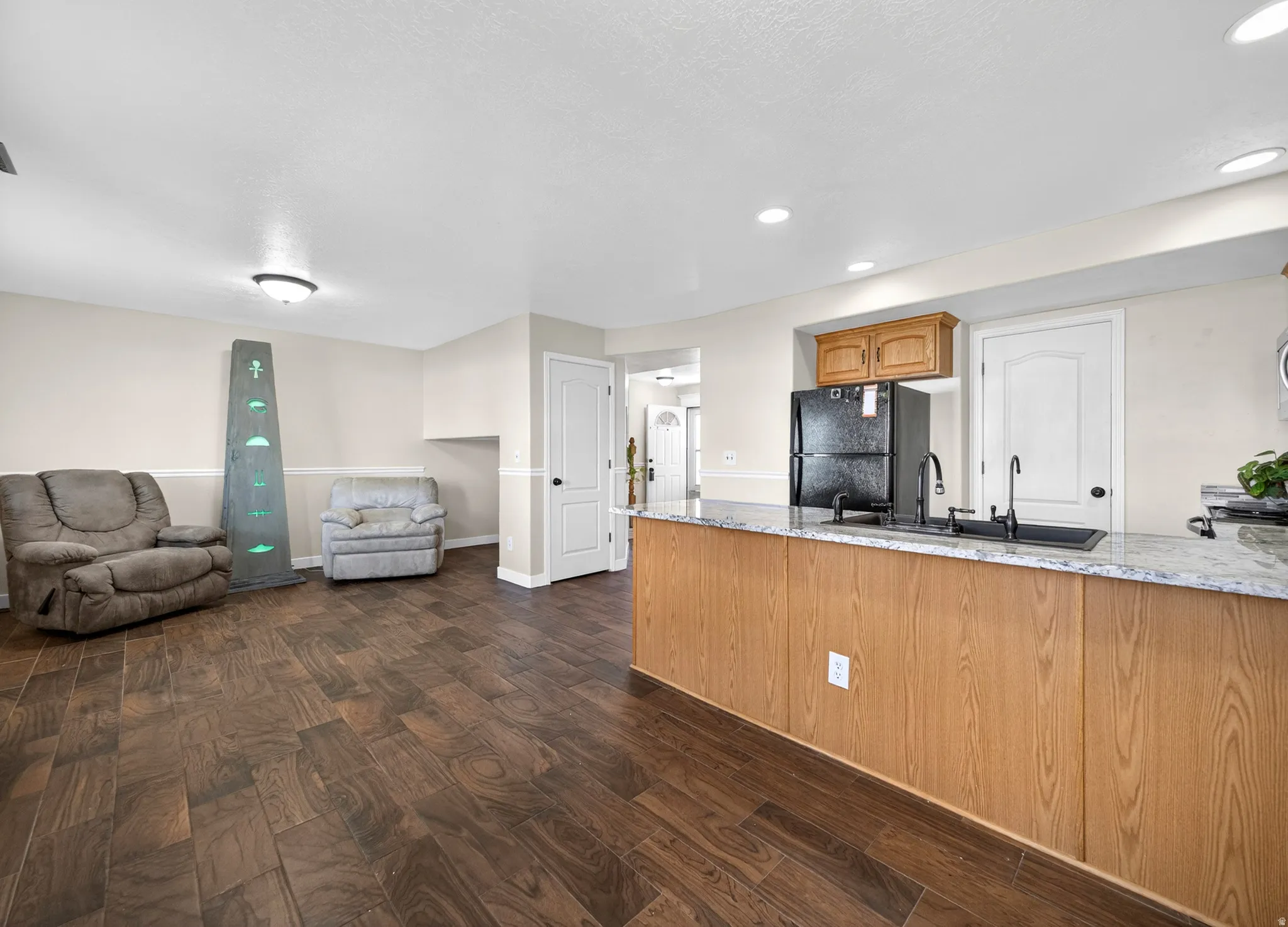 Kitchen featuring dark wood finished floors, freestanding refrigerator, open floor plan, a peninsula, and light stone countertops