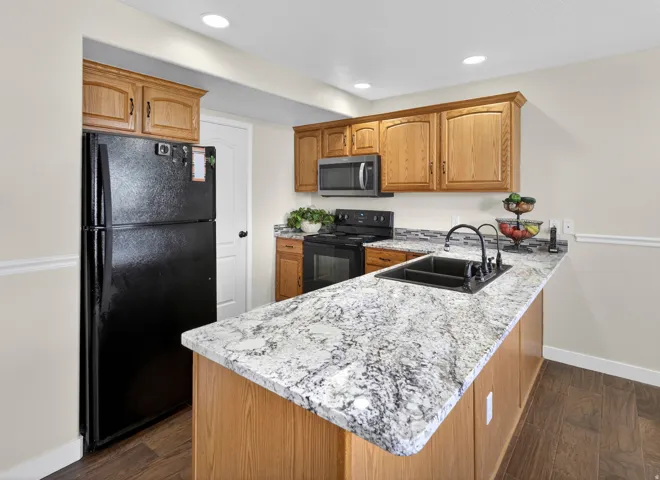 Kitchen with black appliances, a peninsula, dark wood-type flooring, wood finish cabinets, and recessed lighting