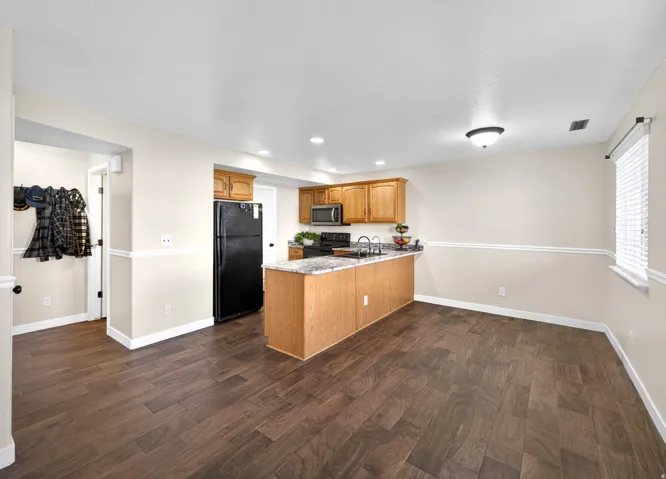 Kitchen featuring a peninsula, dark wood-type flooring, black appliances, recessed lighting, and light stone countertops