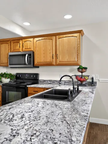Kitchen with black / electric stove, light stone counters, stainless steel microwave, and wood finished floors