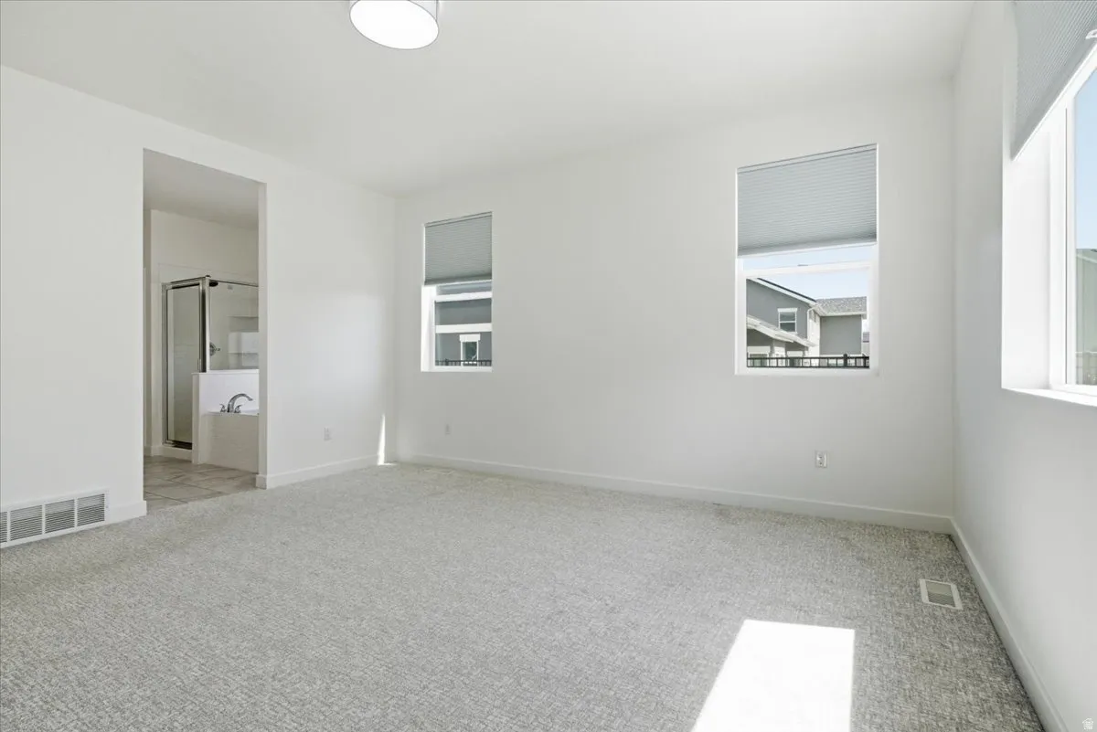 Unfurnished bedroom with light colored carpet, multiple windows, and ensuite bath