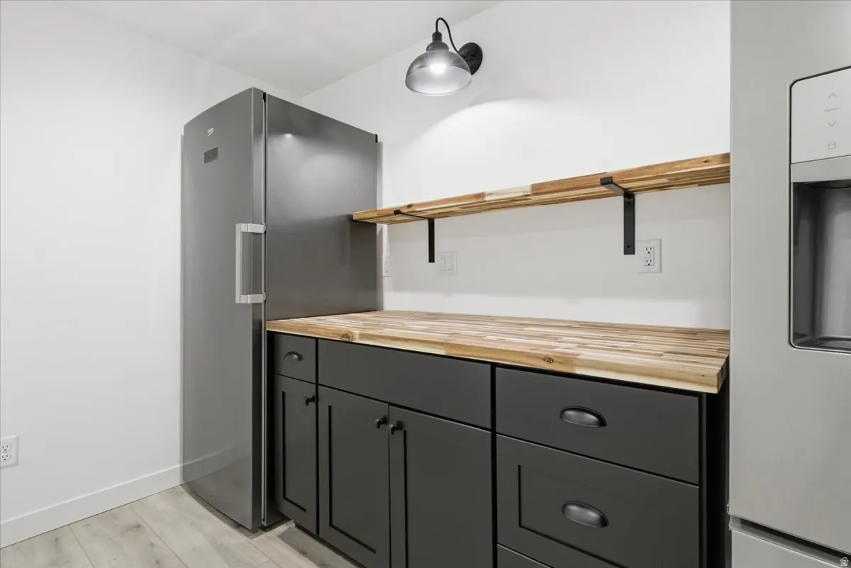 Kitchen featuring butcher block counters, freestanding refrigerator, stainless steel refrigerator with ice dispenser, light wood-style flooring, and open shelves