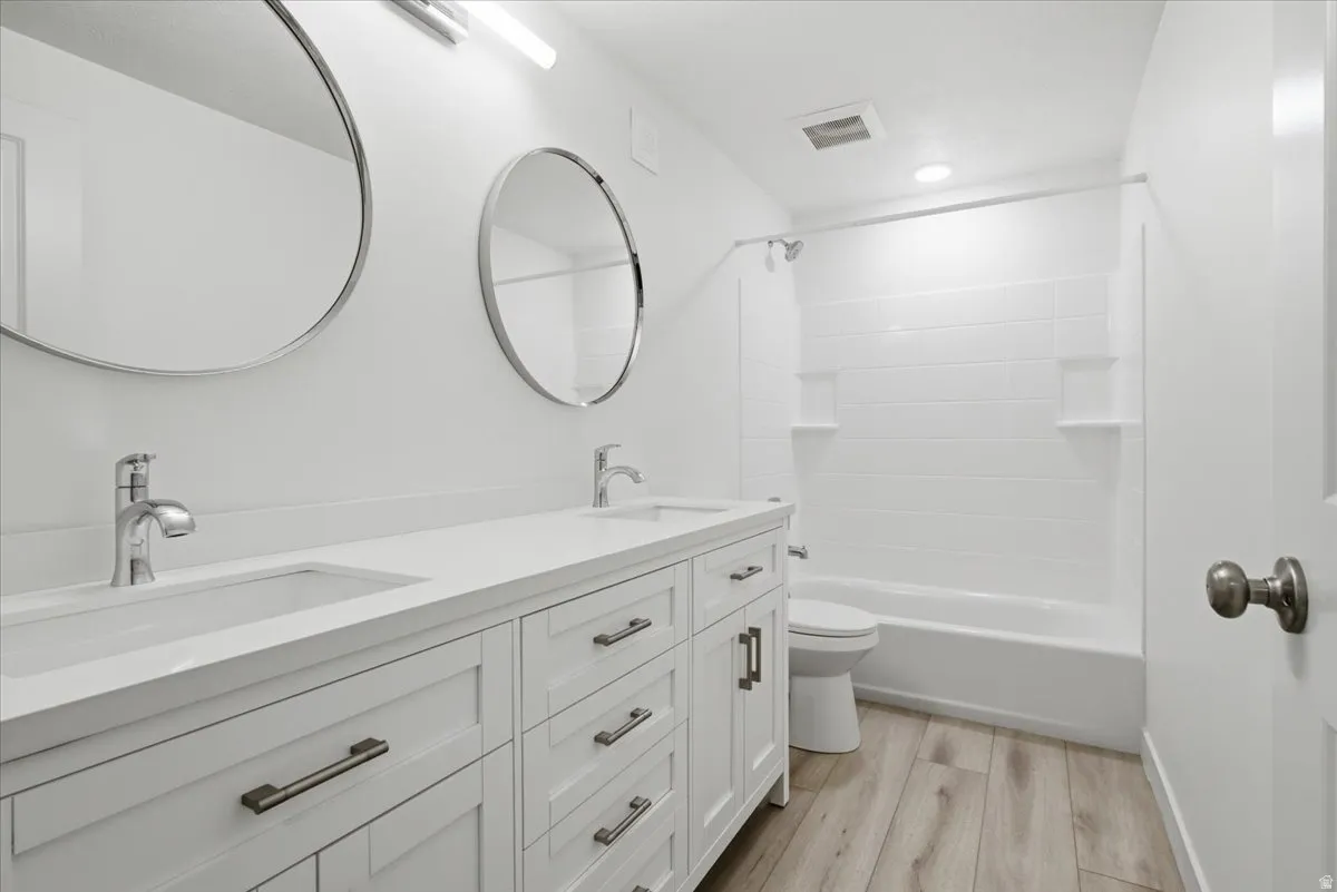 Bathroom featuring double vanity, light wood finished floors, and bathing tub / shower combination