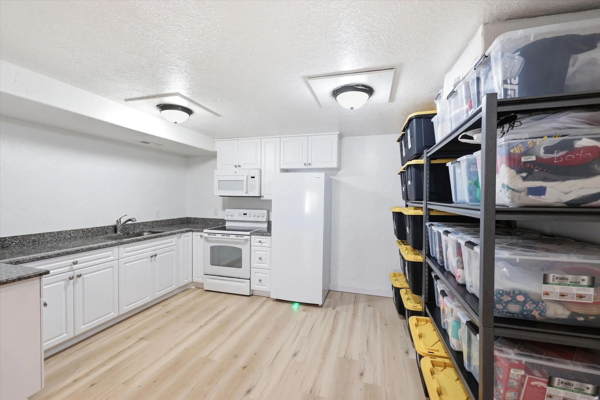 Kitchen with a textured ceiling, white appliances, light wood-style floors, white cabinetry, and dark stone counters