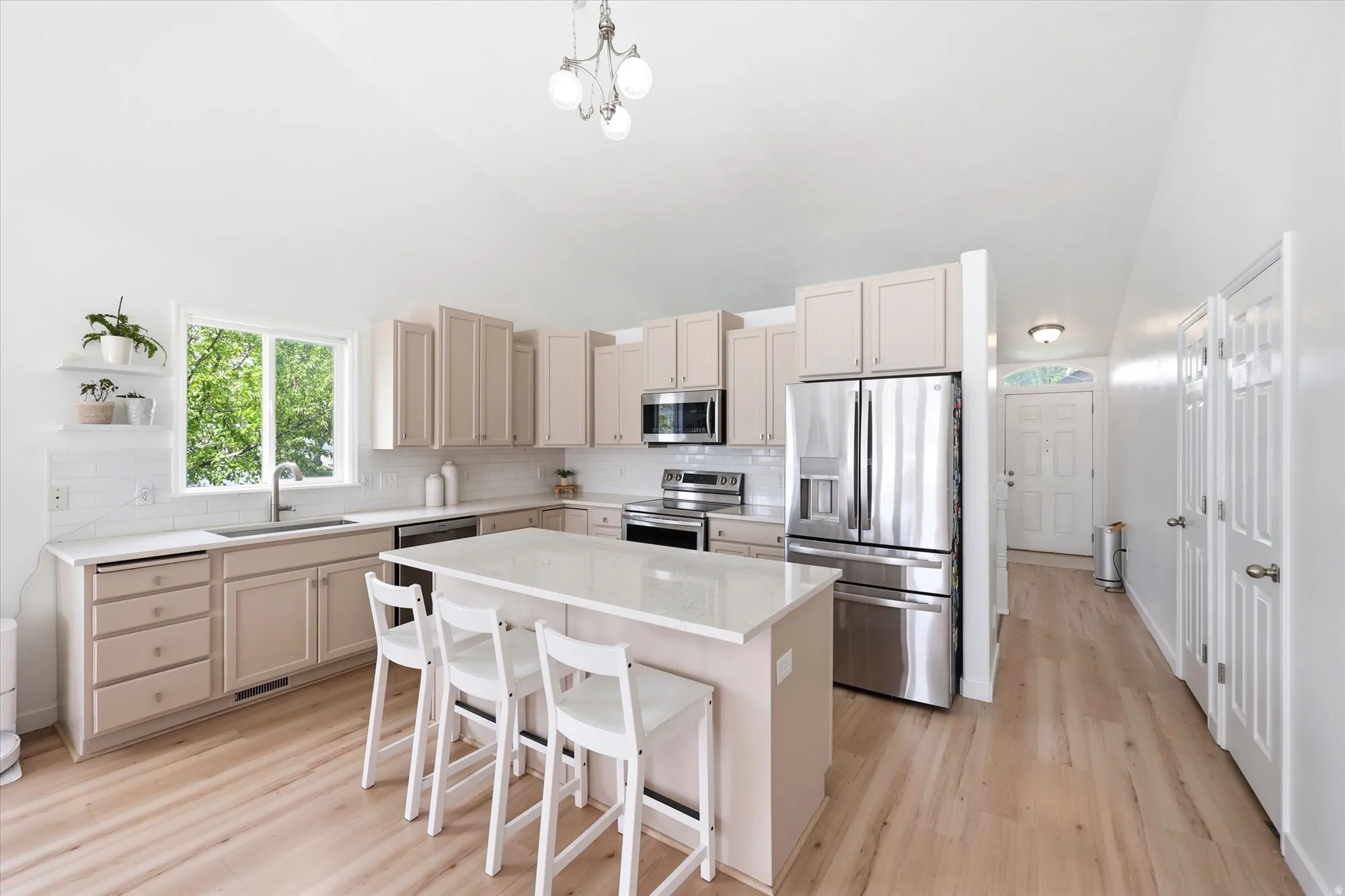 Kitchen with stainless steel appliances, lofted ceiling, light wood-style flooring, a breakfast bar, and light stone countertops