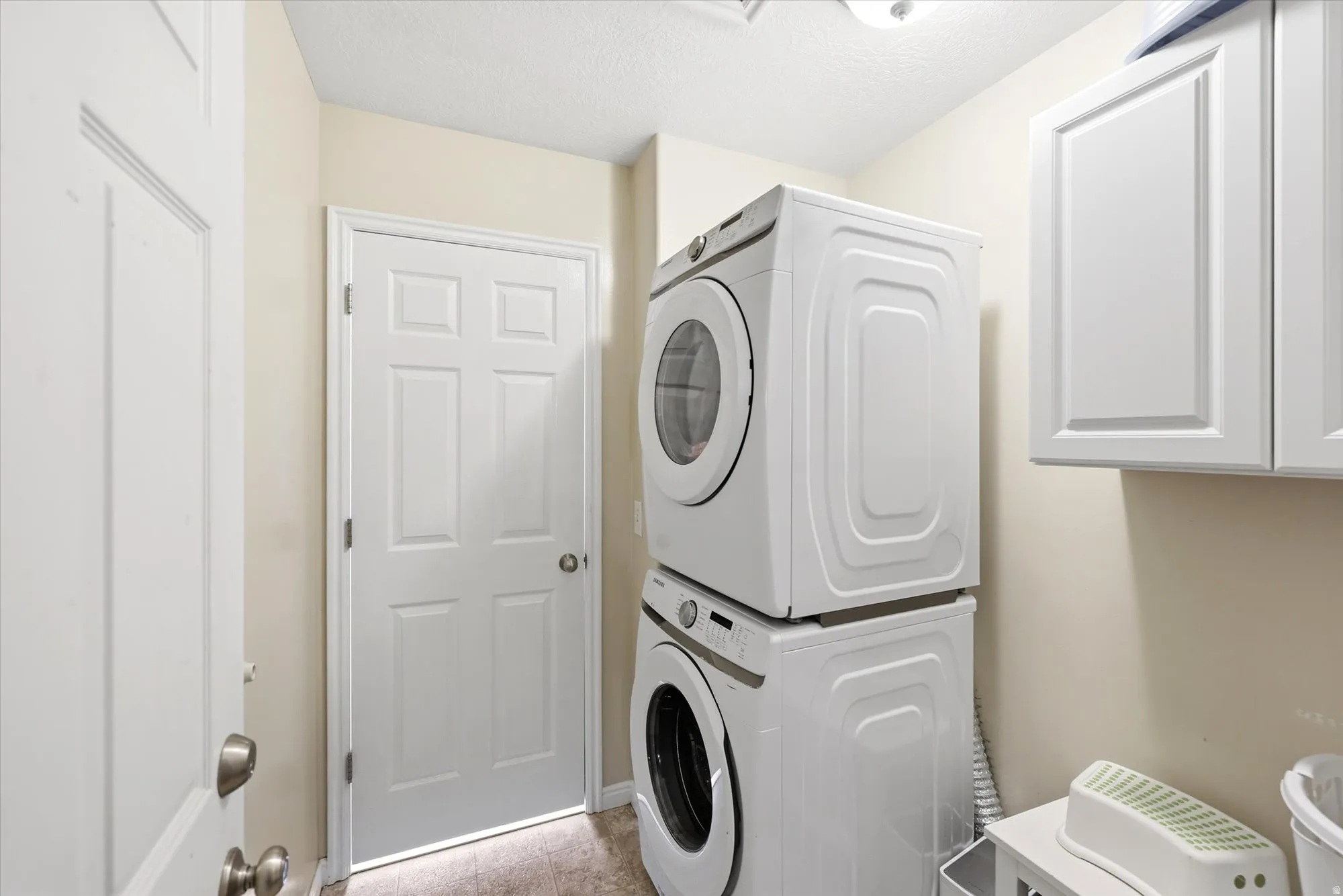 Laundry room with stacked washer and clothes dryer, a textured ceiling, and light tile patterned floors