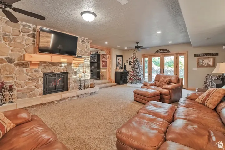 Carpeted living room with a ceiling fan, a textured ceiling, french doors, a fireplace, and recessed lighting