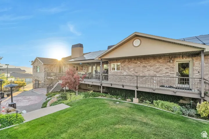 Rear view of house featuring a chimney, a yard, a wooden deck, brick siding, and solar panels