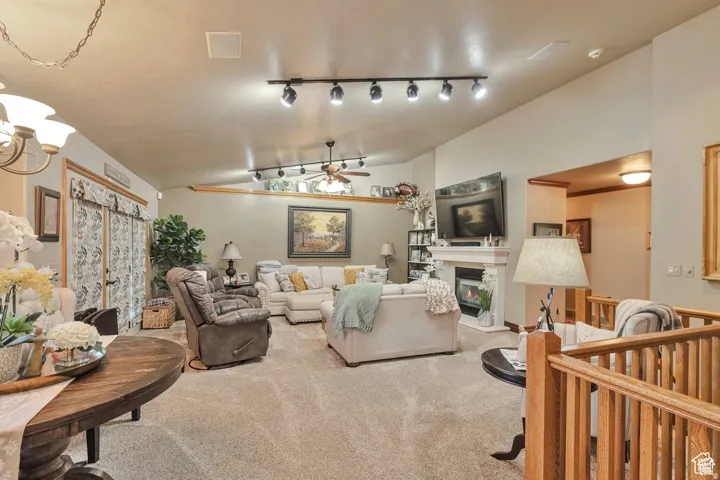 Living area featuring vaulted ceiling, ceiling fan, carpet floors, a glass covered fireplace, and hanging lights