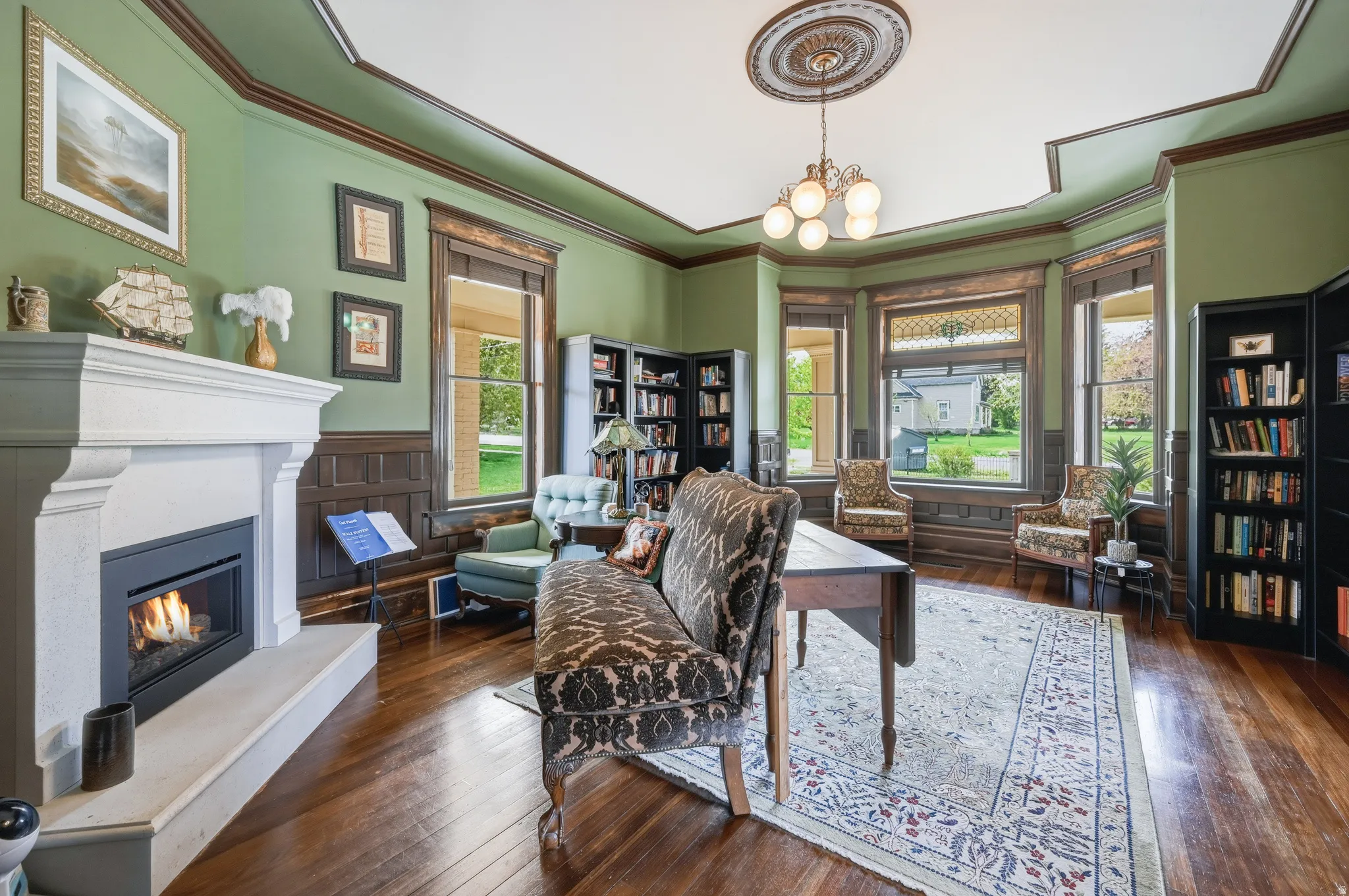 Library with wainscoting, dark wood flooring, Cast Stone fireplace, crown molding, and a chandelier with ceiling medallion
