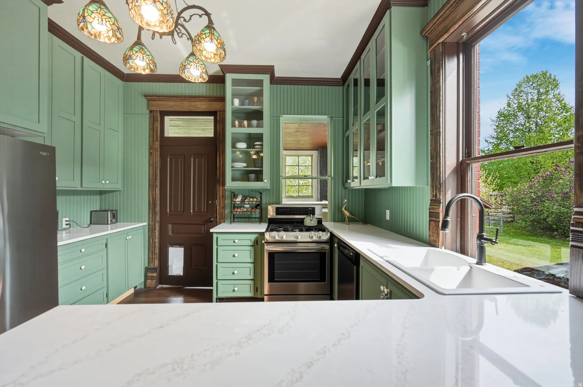 Kitchen with green cabinetry, stainless steel appliances, glass fronted cabinets, crown molding, and quartz countertops