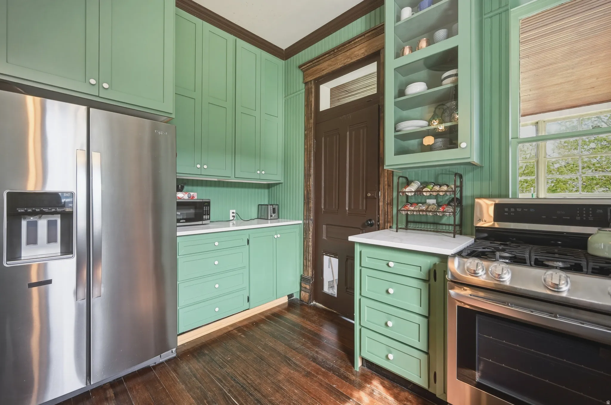 Kitchen featuring green cabinetry, stainless steel appliances, dark wood flooring, glass fronted cabinets, and ornamental molding