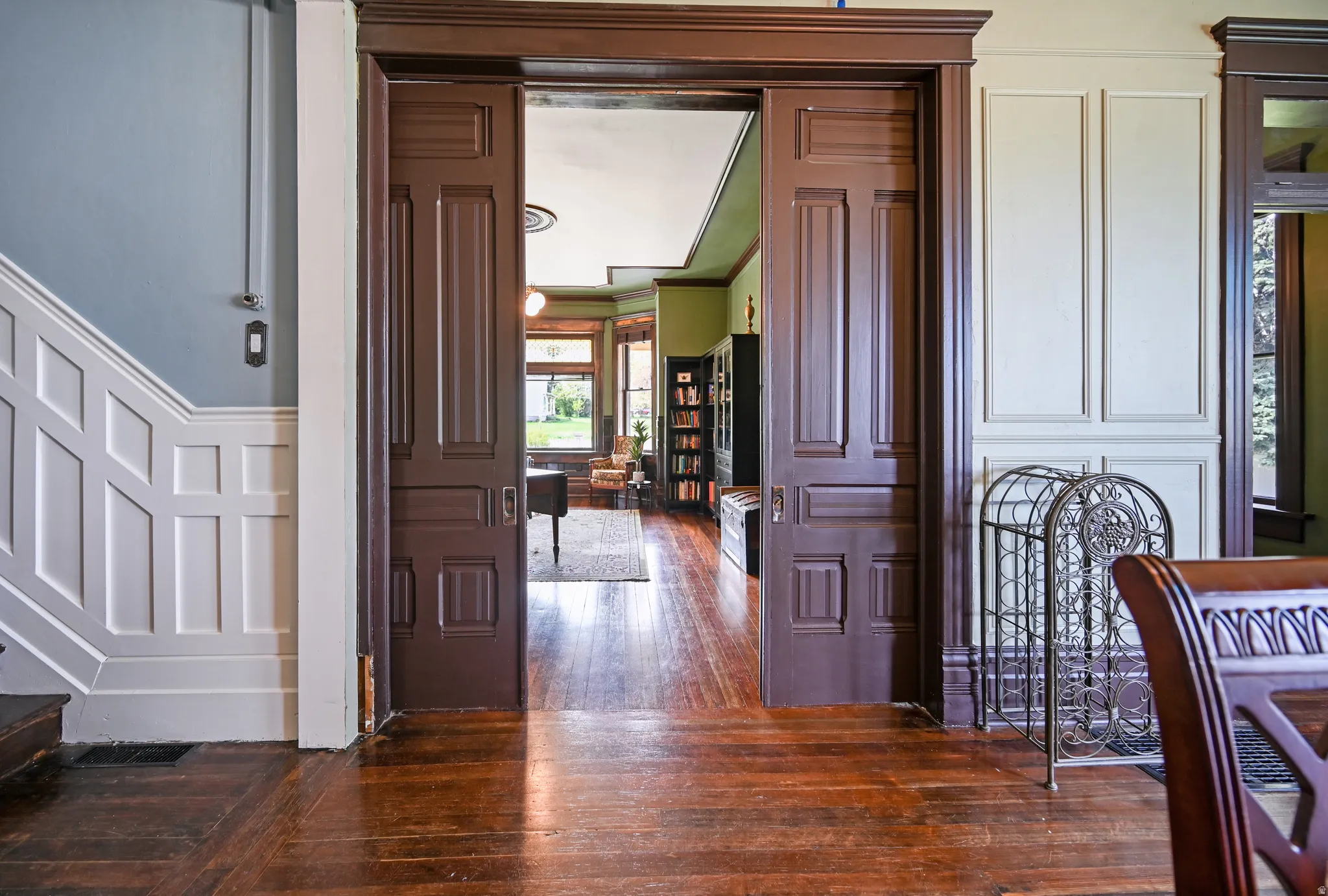 Pocket door entry into library with dark wood flooring, a decorative wall, and ornamental molding