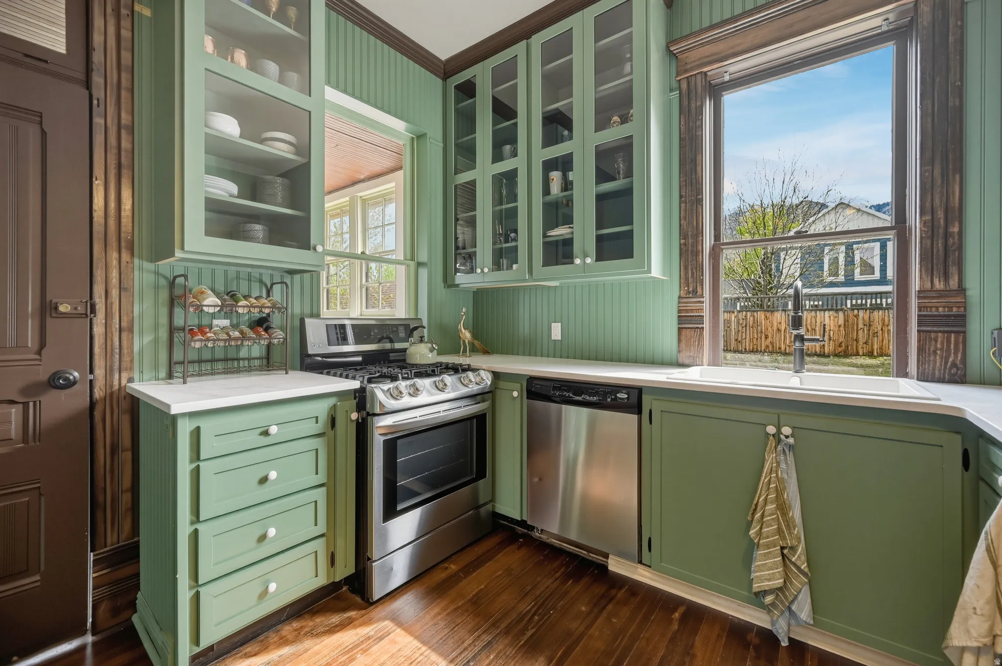 Kitchen with green cabinetry, stainless steel appliances, glass insert cabinets, dark wood flooring, and crown molding