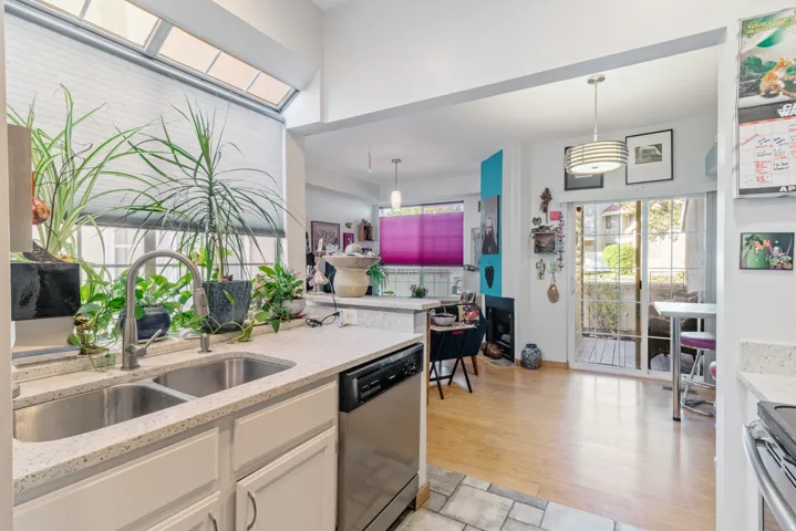 Kitchen featuring light stone counters, stainless steel appliances, decorative light fixtures, white cabinetry, and light wood-style flooring