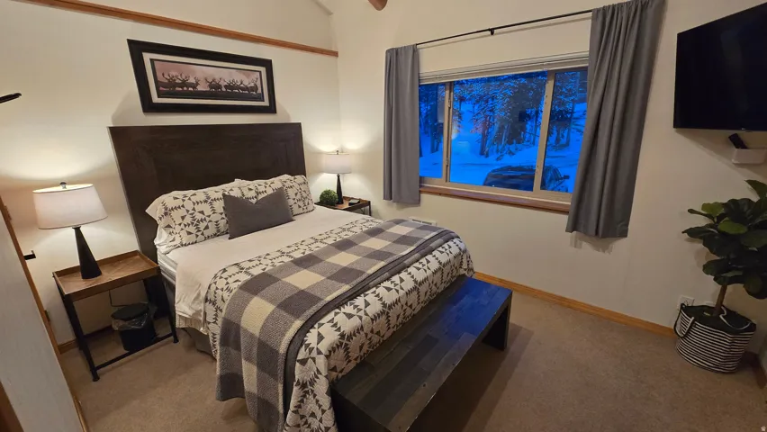 Bedroom featuring a dark wood headboard, two bedside tables with lamps, a window with grey curtains, and carpet flooring