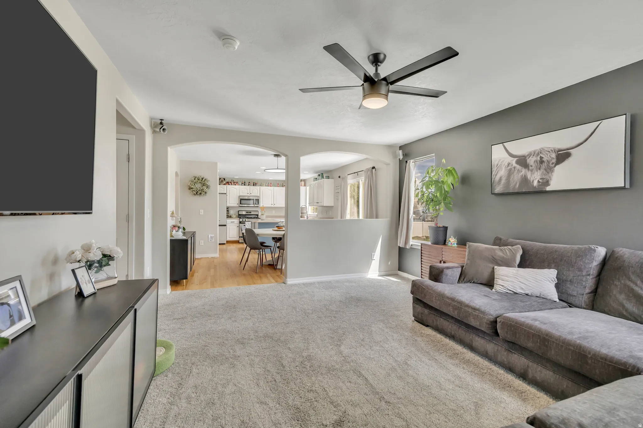 Living room with arched walkways, ceiling fan, and light carpet