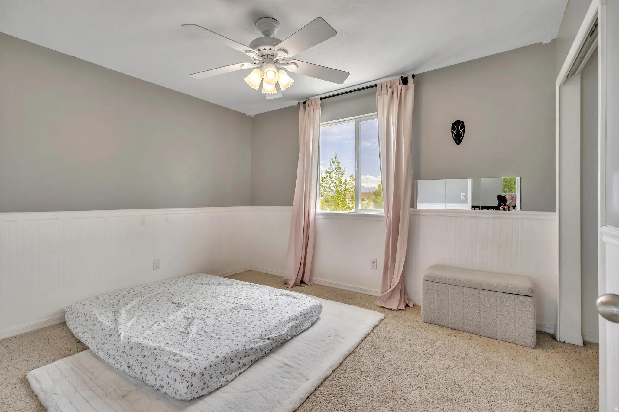 Bedroom with light colored carpet, ceiling fan, and a wainscoted wall