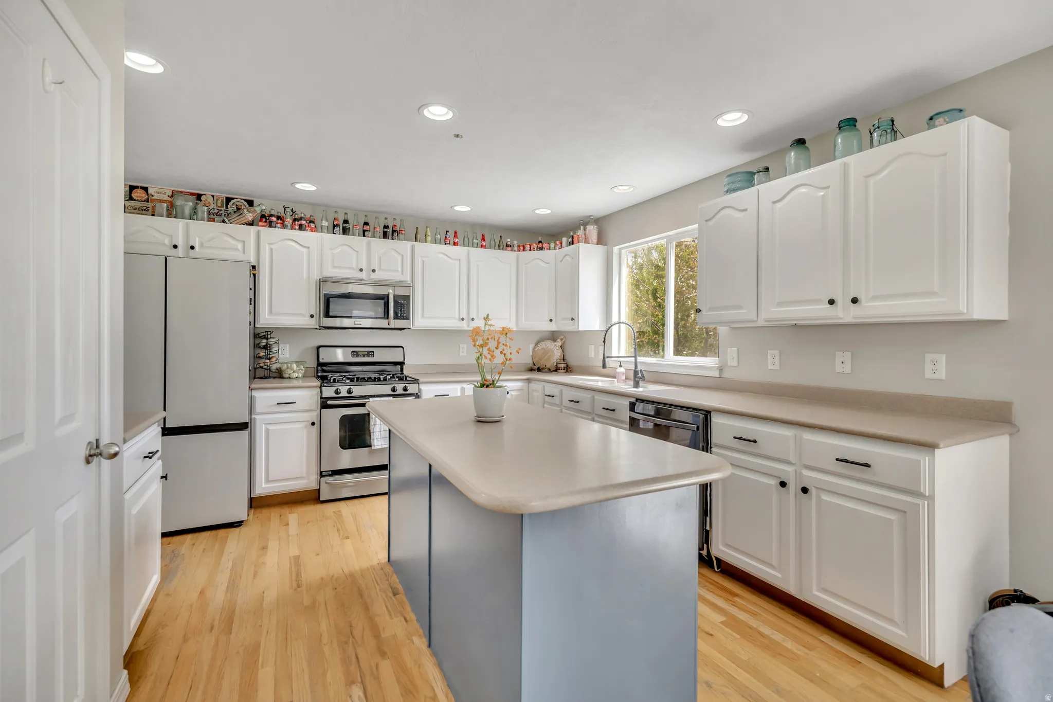 Kitchen with stainless steel appliances, light countertops, white cabinets, light wood finished floors, and recessed lighting