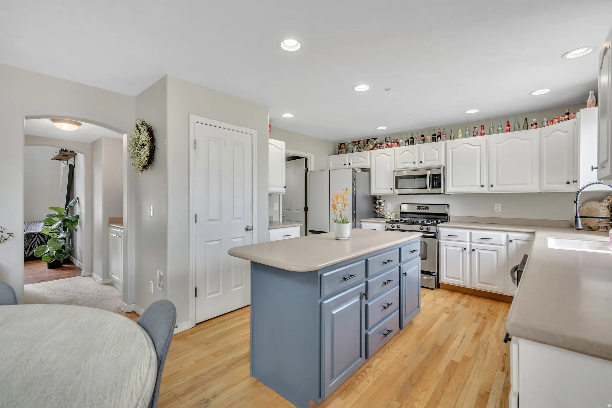 Kitchen with two tone cabinets, arched walkways, stainless steel appliances, light wood-type flooring, and a kitchen island