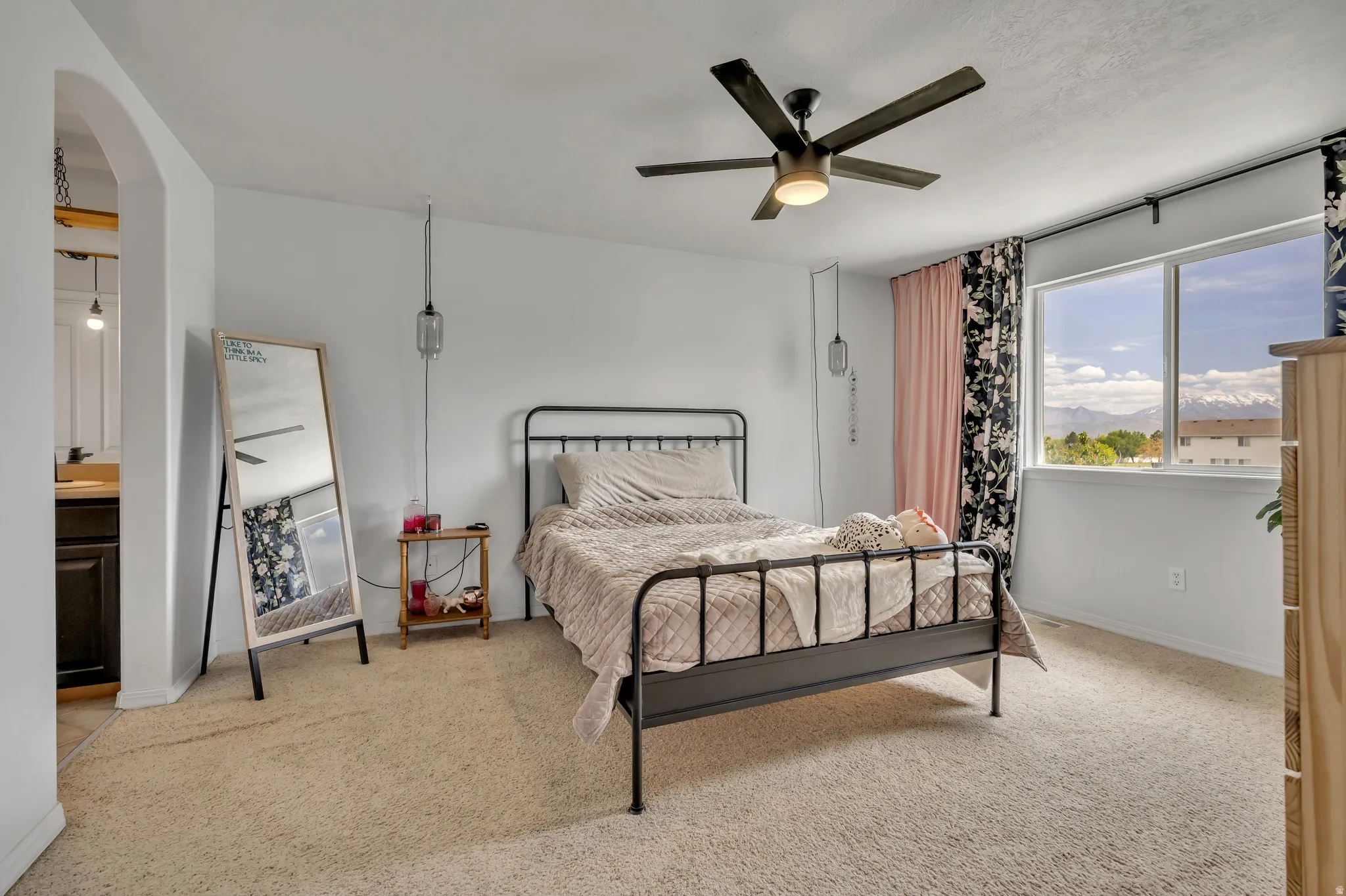 Bedroom with light colored carpet, ceiling fan, arched walkways, and connected bathroom