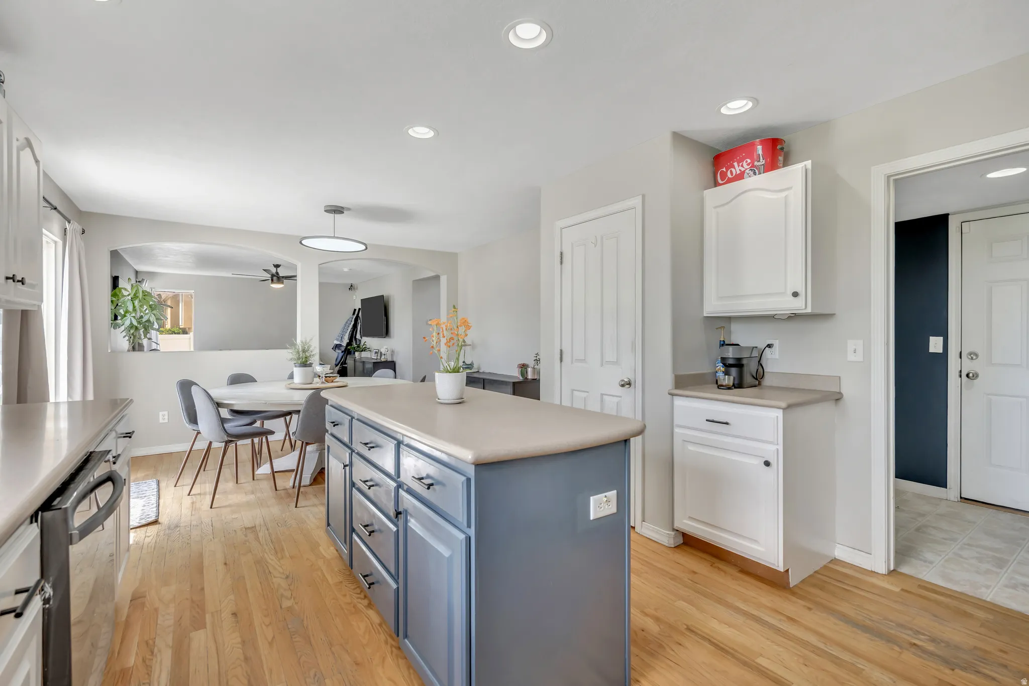 Dual tone kitchen featuring arched walkways, light countertops, two tone cabinetry, a kitchen island, and stainless steel dishwasher