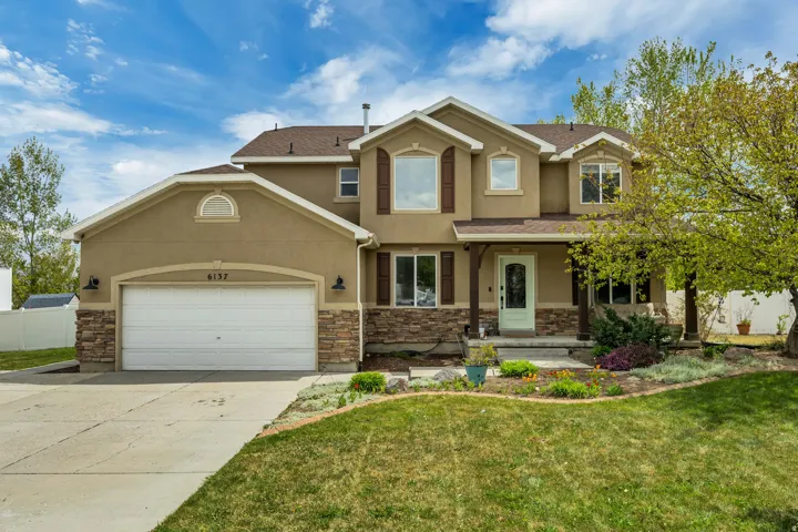 View of front of house with covered porch, stucco siding, stone siding, driveway, and an attached garage