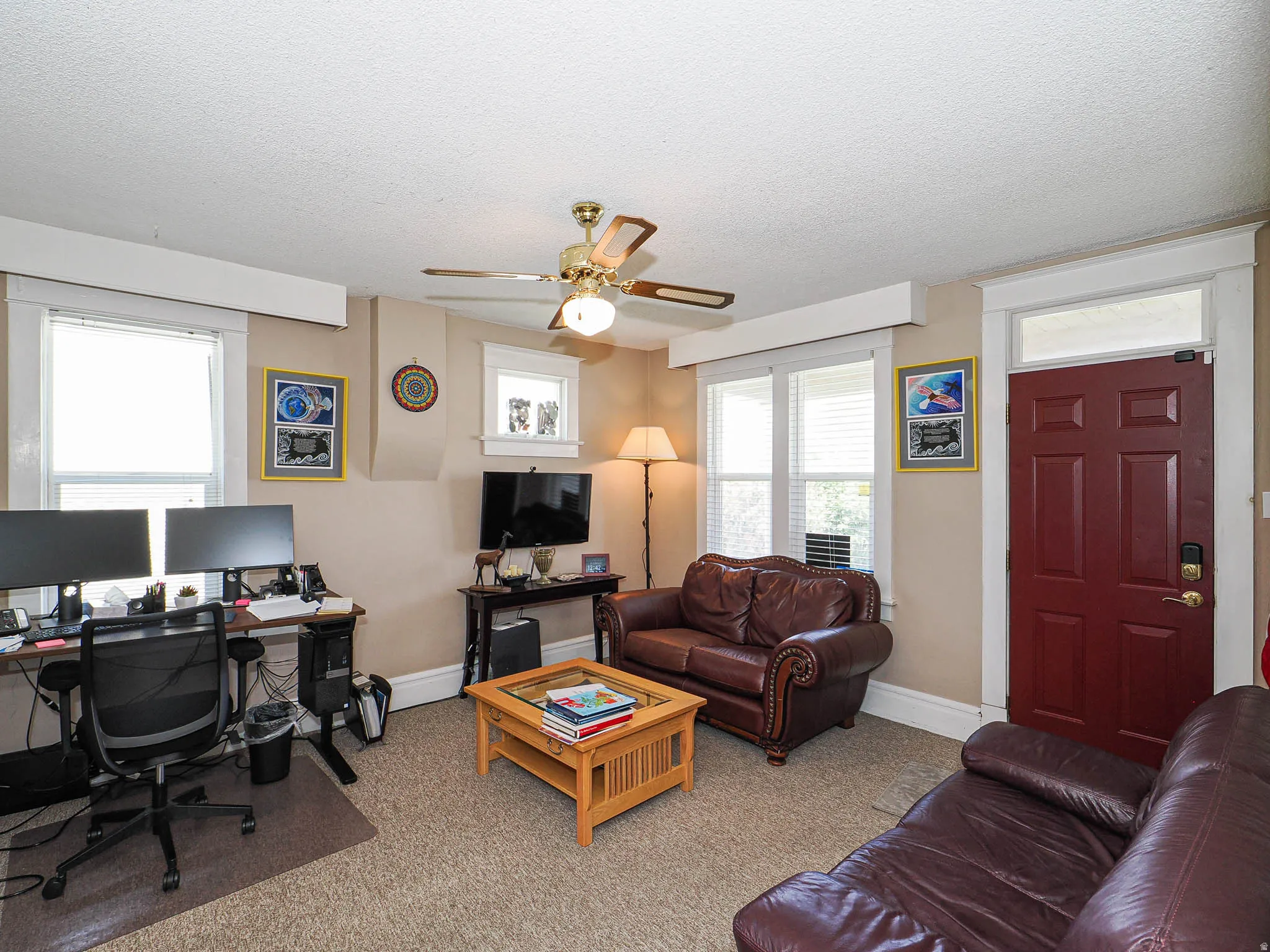 Living area featuring a desk, ceiling fan, light colored carpet, and a textured ceiling