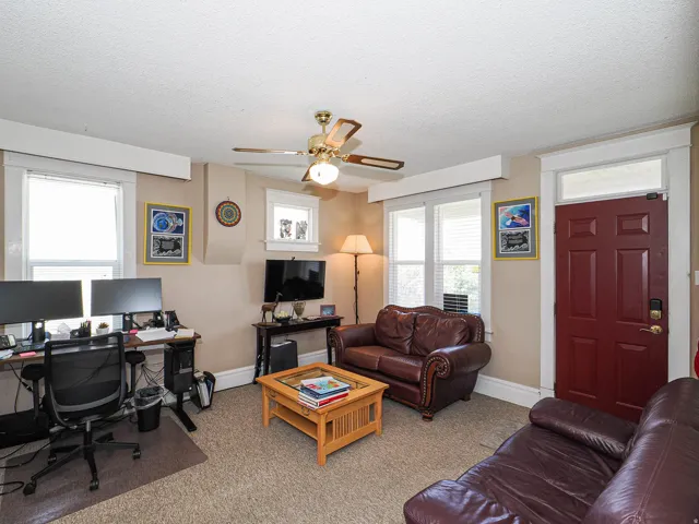 Living area featuring a desk, ceiling fan, light colored carpet, and a textured ceiling