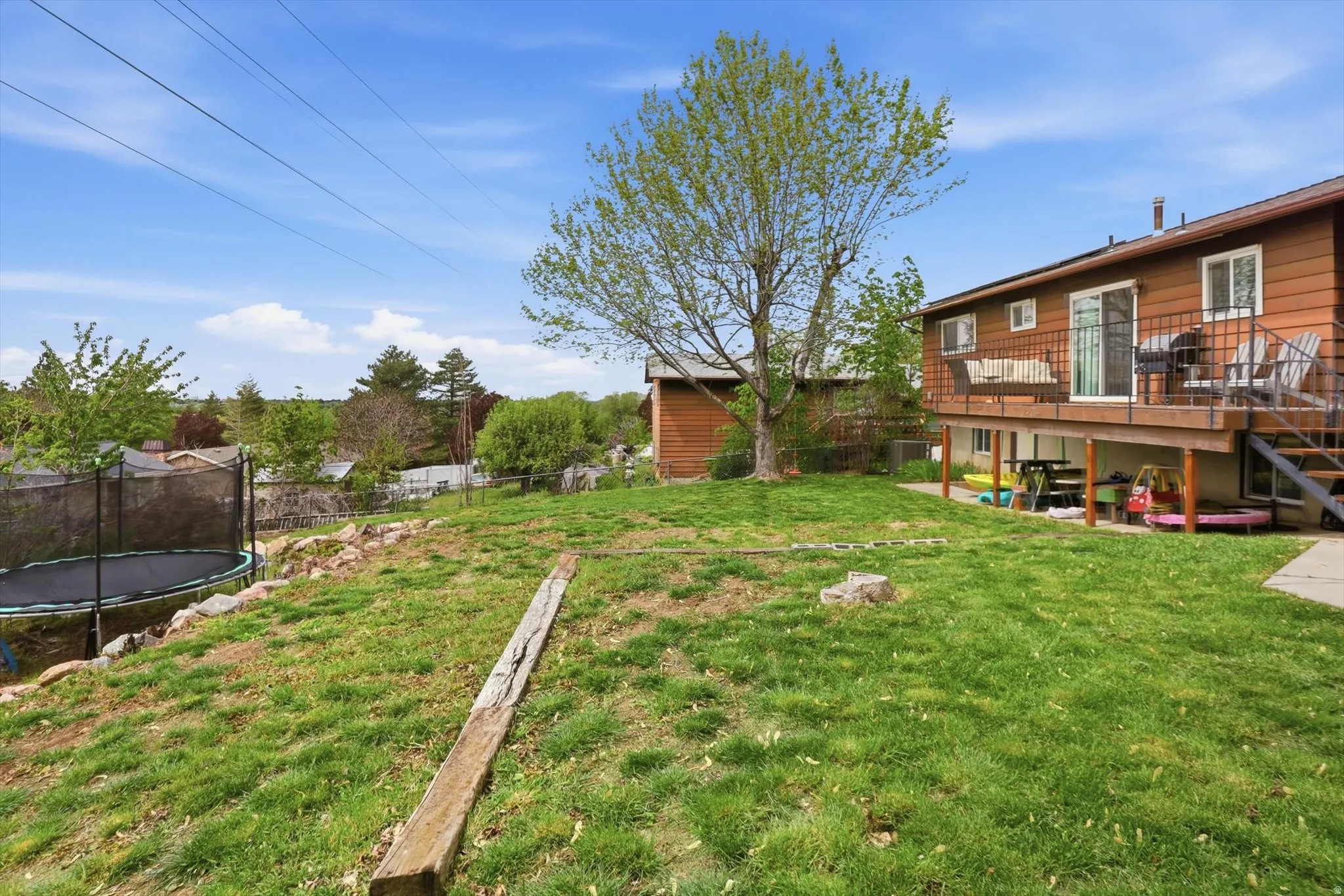 Fenced backyard featuring a trampoline, a deck, and a patio area