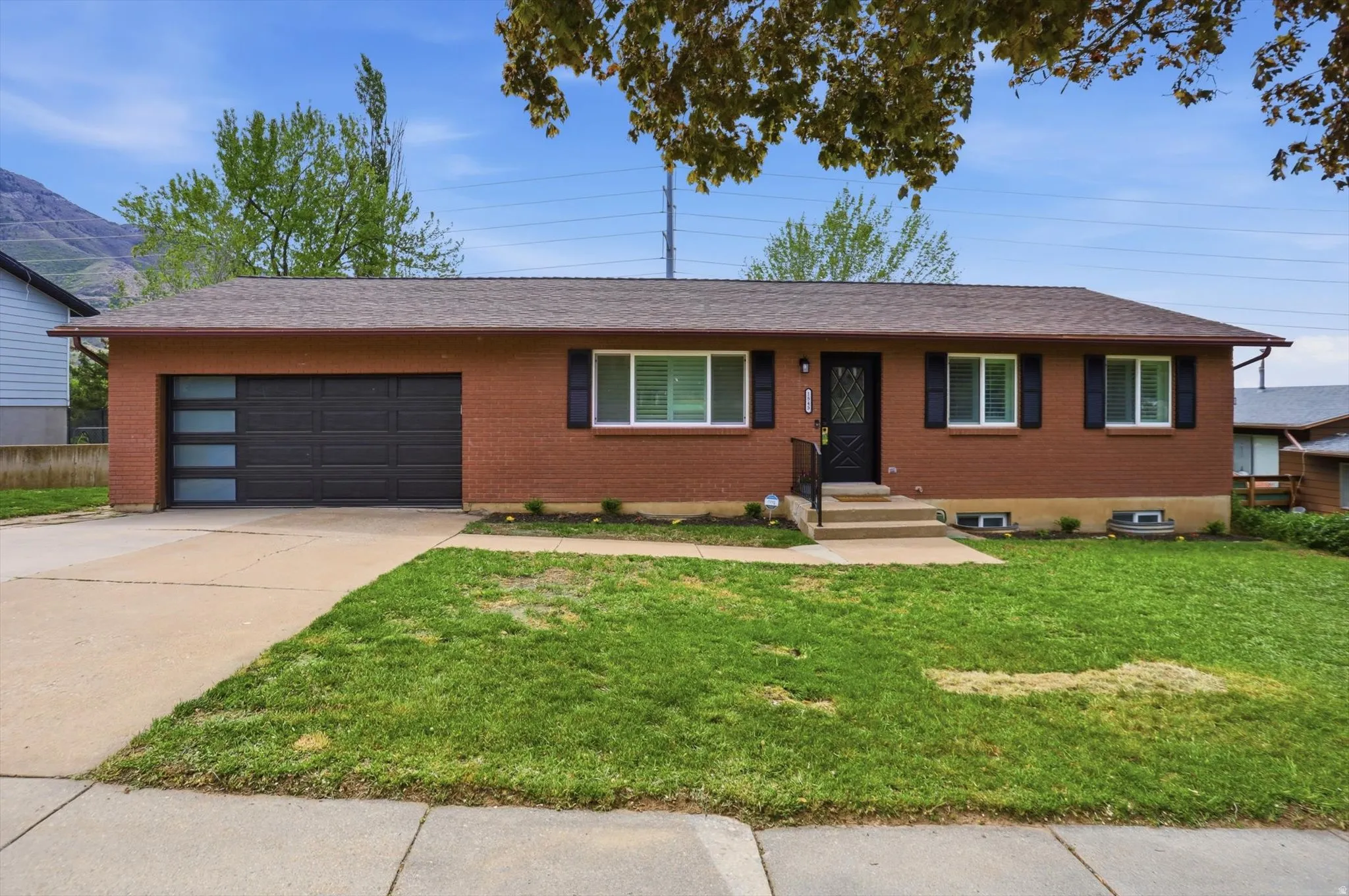 Ranch-style home with brick siding, a front yard, concrete driveway, a garage, and a shingled roof