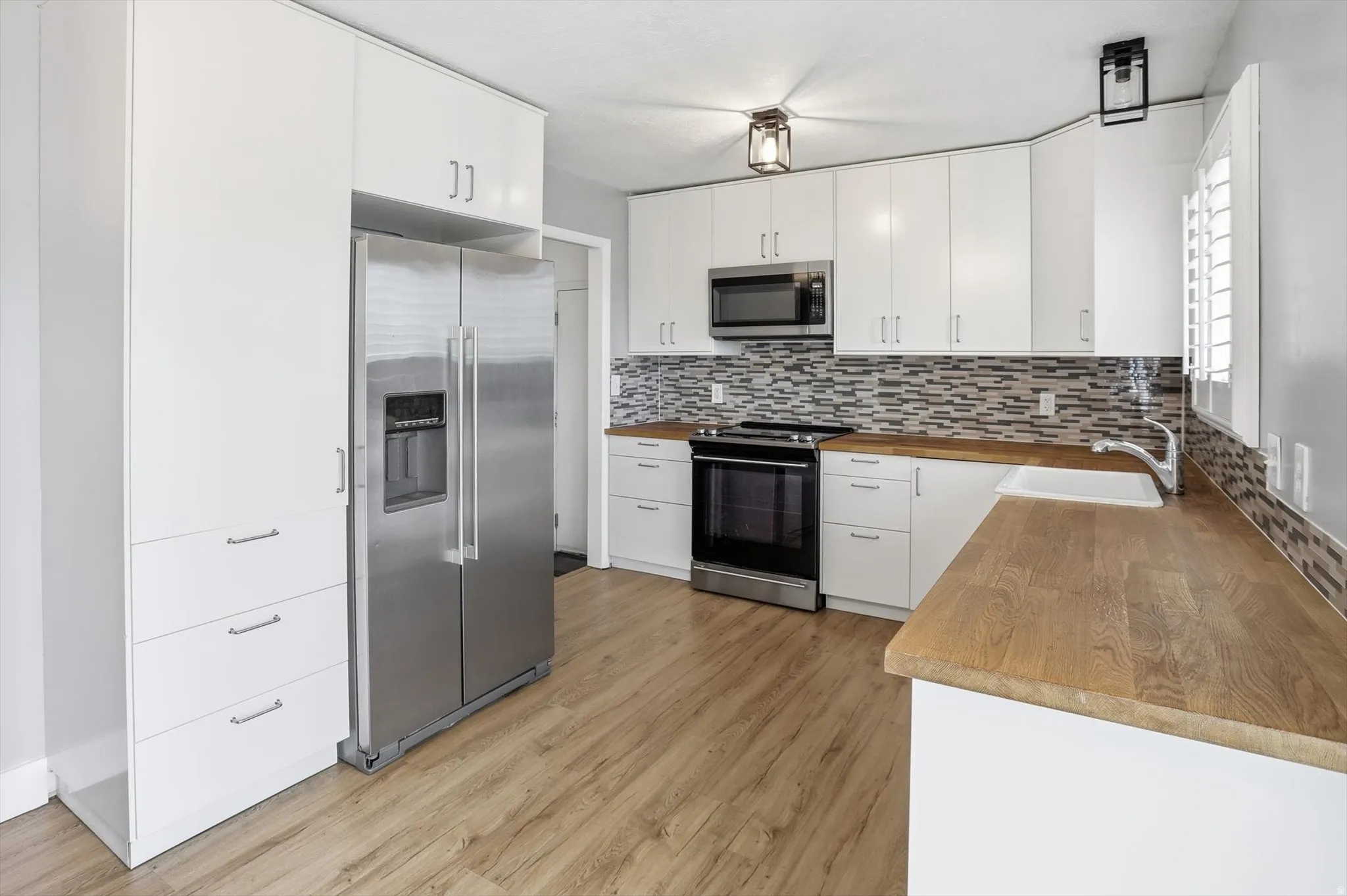 Kitchen with stainless steel appliances, white cabinetry, butcher block countertops, light wood-type flooring, and tasteful backsplash
