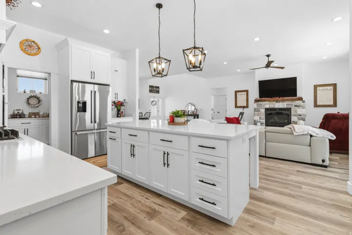 Kitchen with an island with sink, stainless steel appliances, open floor plan, white cabinetry, and a stone fireplace