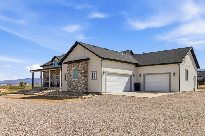 View of front of home with driveway, covered porch, an attached garage, a shingled roof, and stone siding