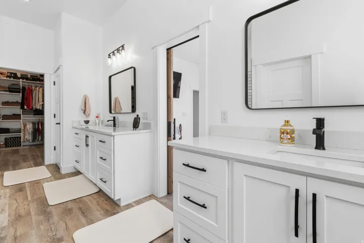 Full bath featuring a spacious closet, light wood finished floors, and two vanities