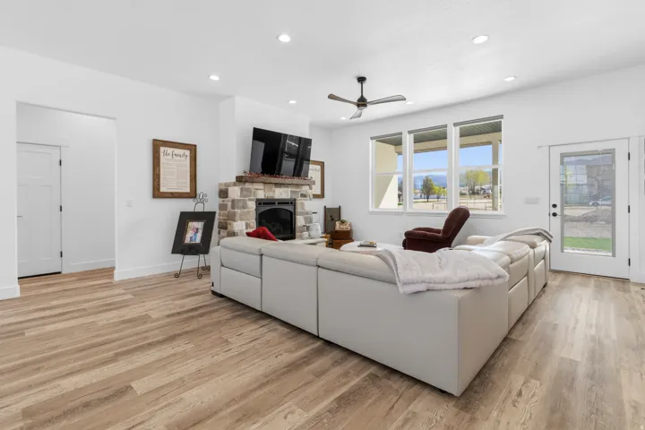 Living room featuring a stone fireplace, light wood-type flooring, recessed lighting, and ceiling fan