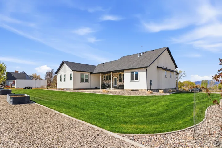 Back of house with a lawn, a shingled roof, stone siding, and a patio