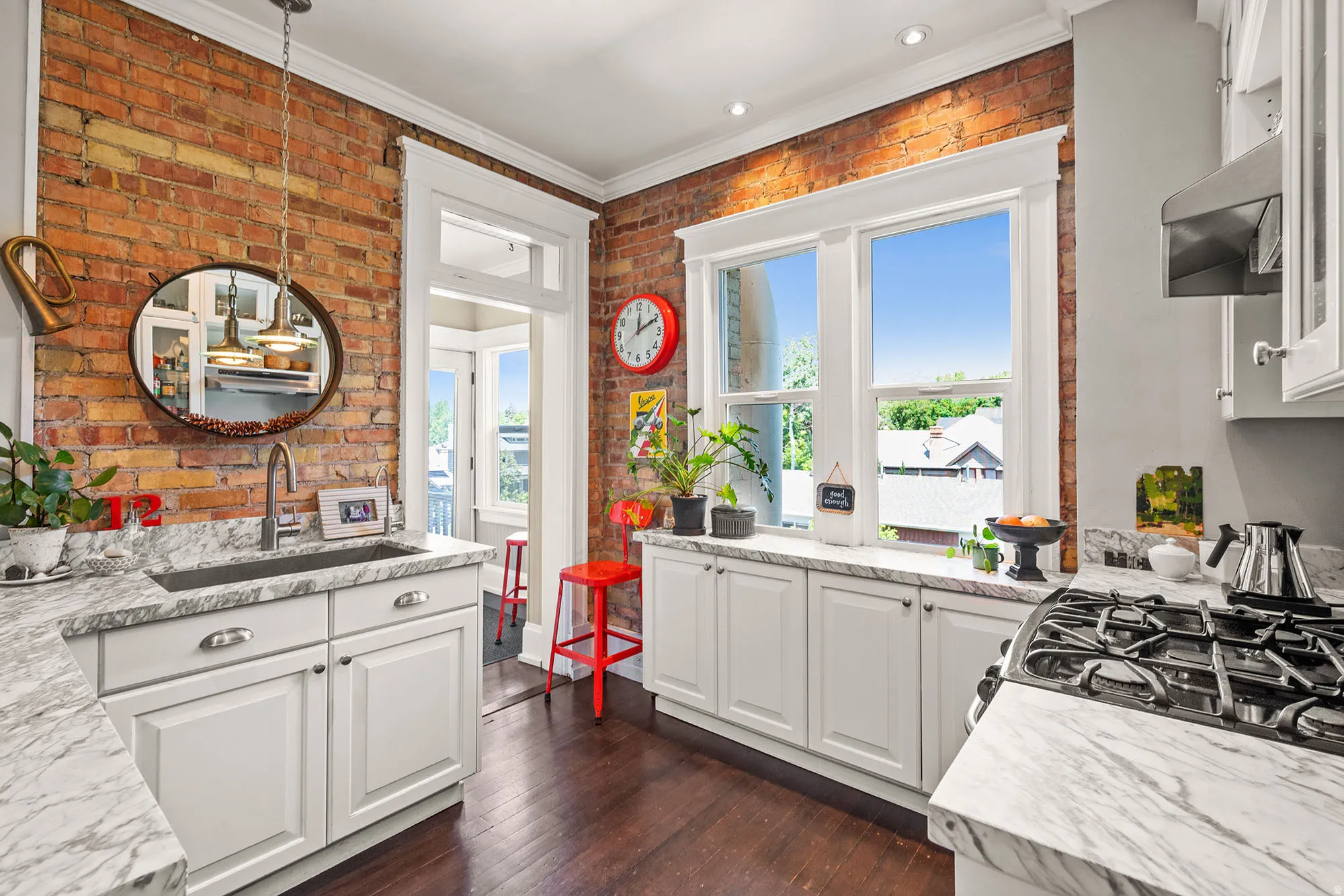 Kitchen featuring dark wood-style flooring, white cabinetry, crown molding, ventilation hood, and brick wall