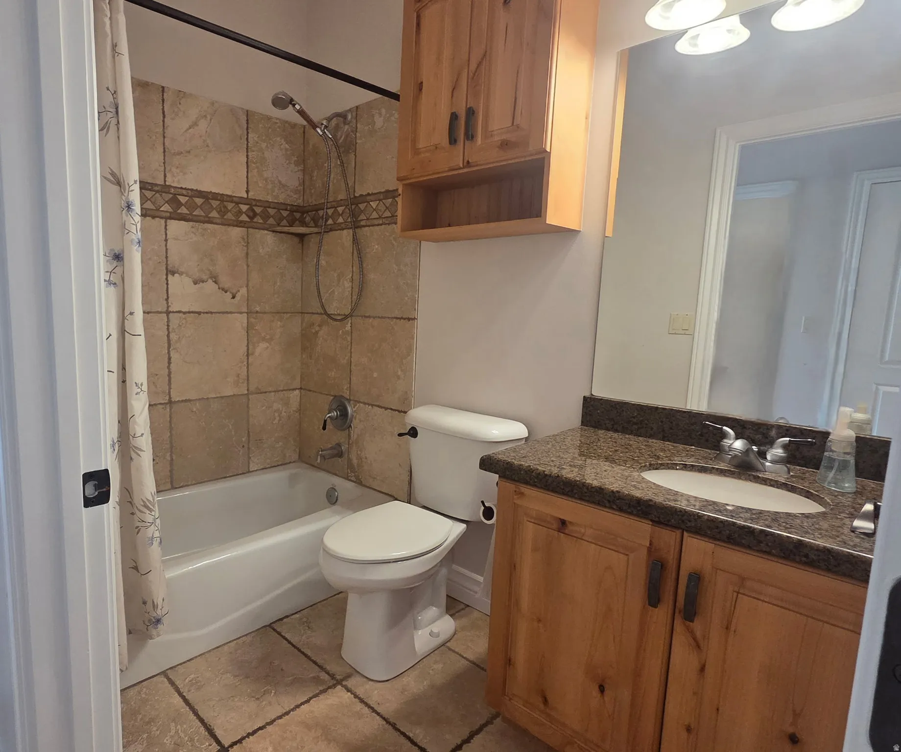 Full bathroom featuring a tub/shower combination with travertine surround, vanity with granite countertop, and wood cabinetry