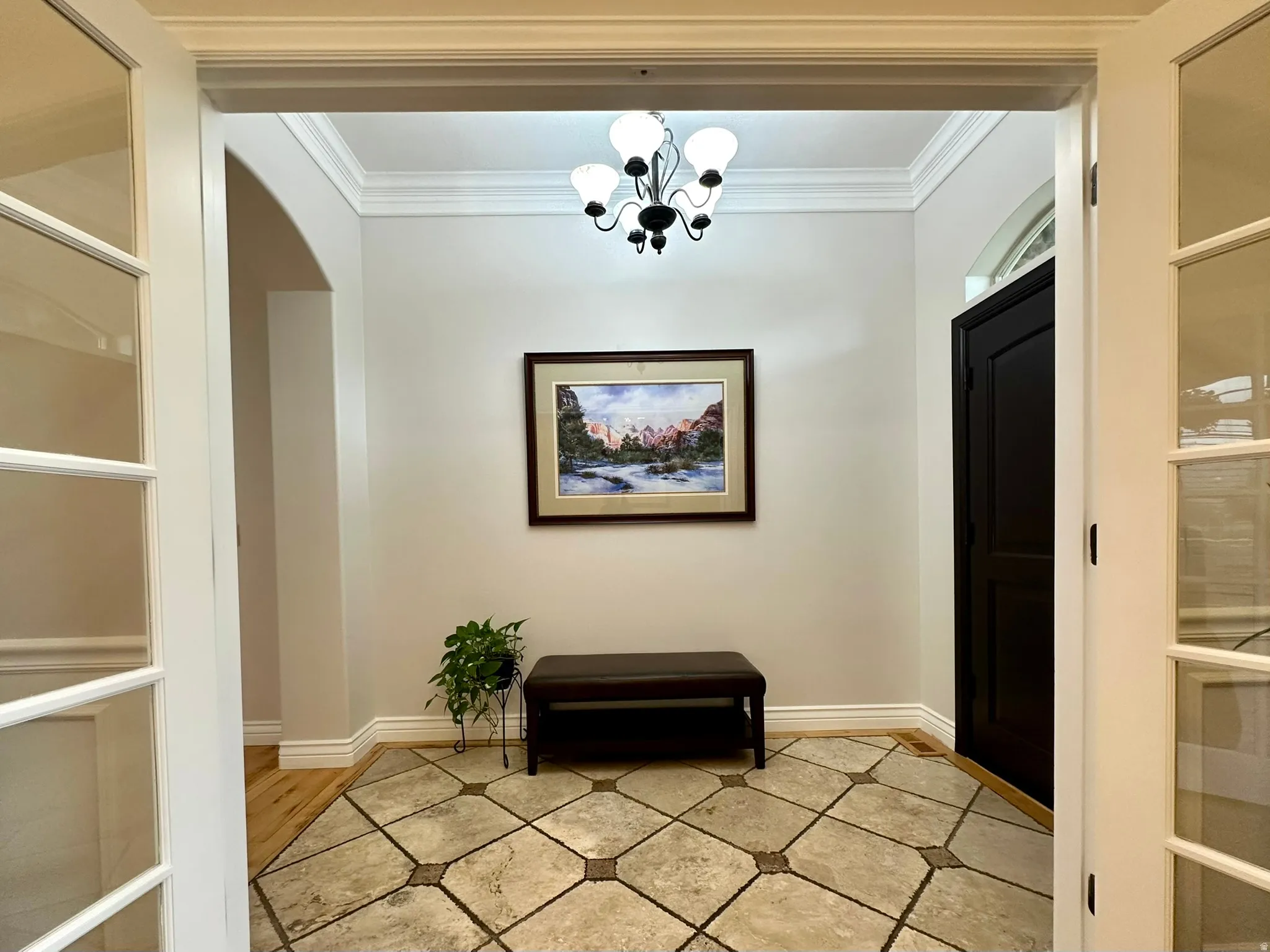 Entryway featuring travertine flooring, a black paneled door with an arched transom, and an ornate ceiling light fixture