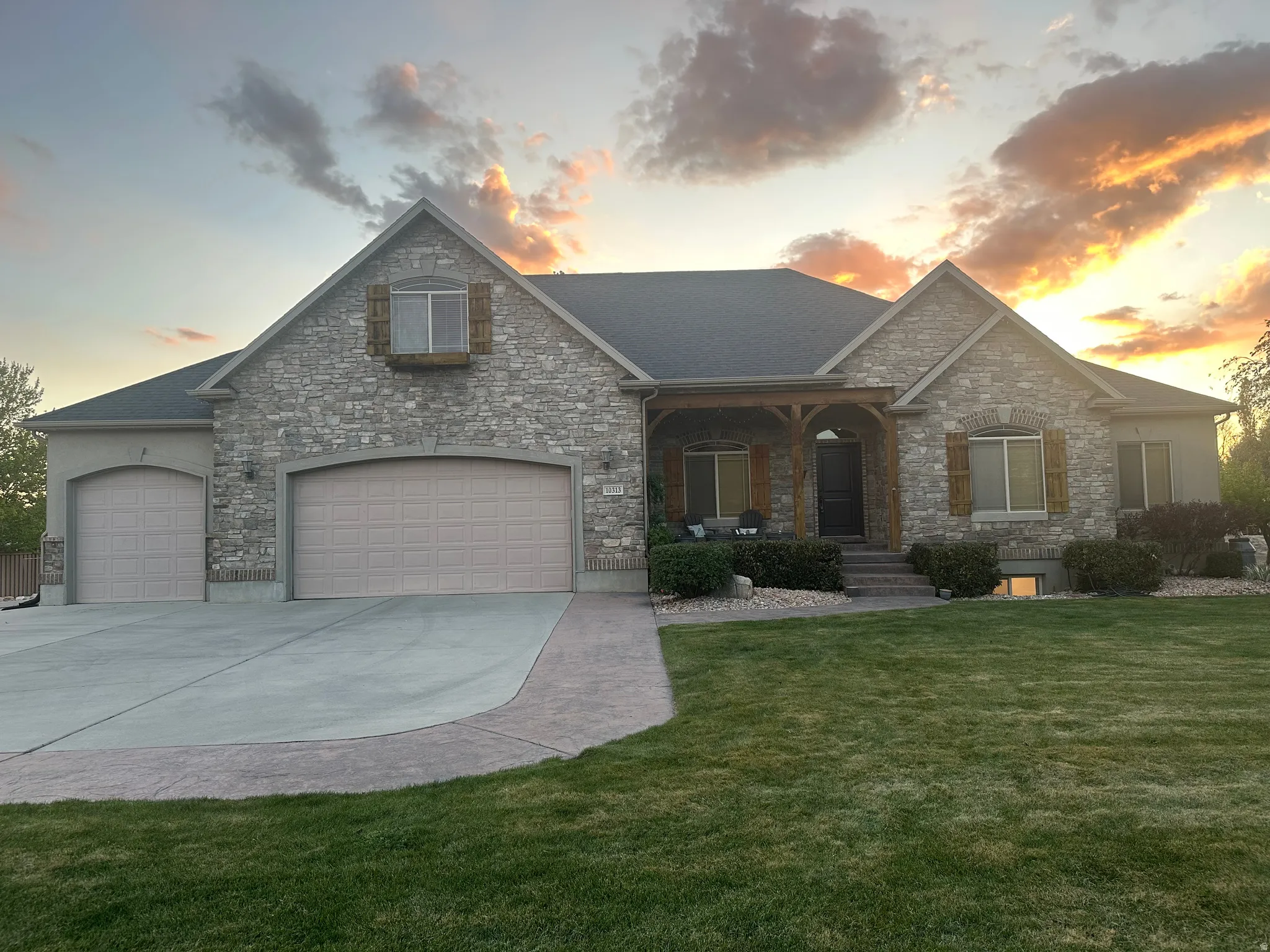 Craftsman-style home with covered porch, stone siding, a front yard, concrete driveway, and a garage
