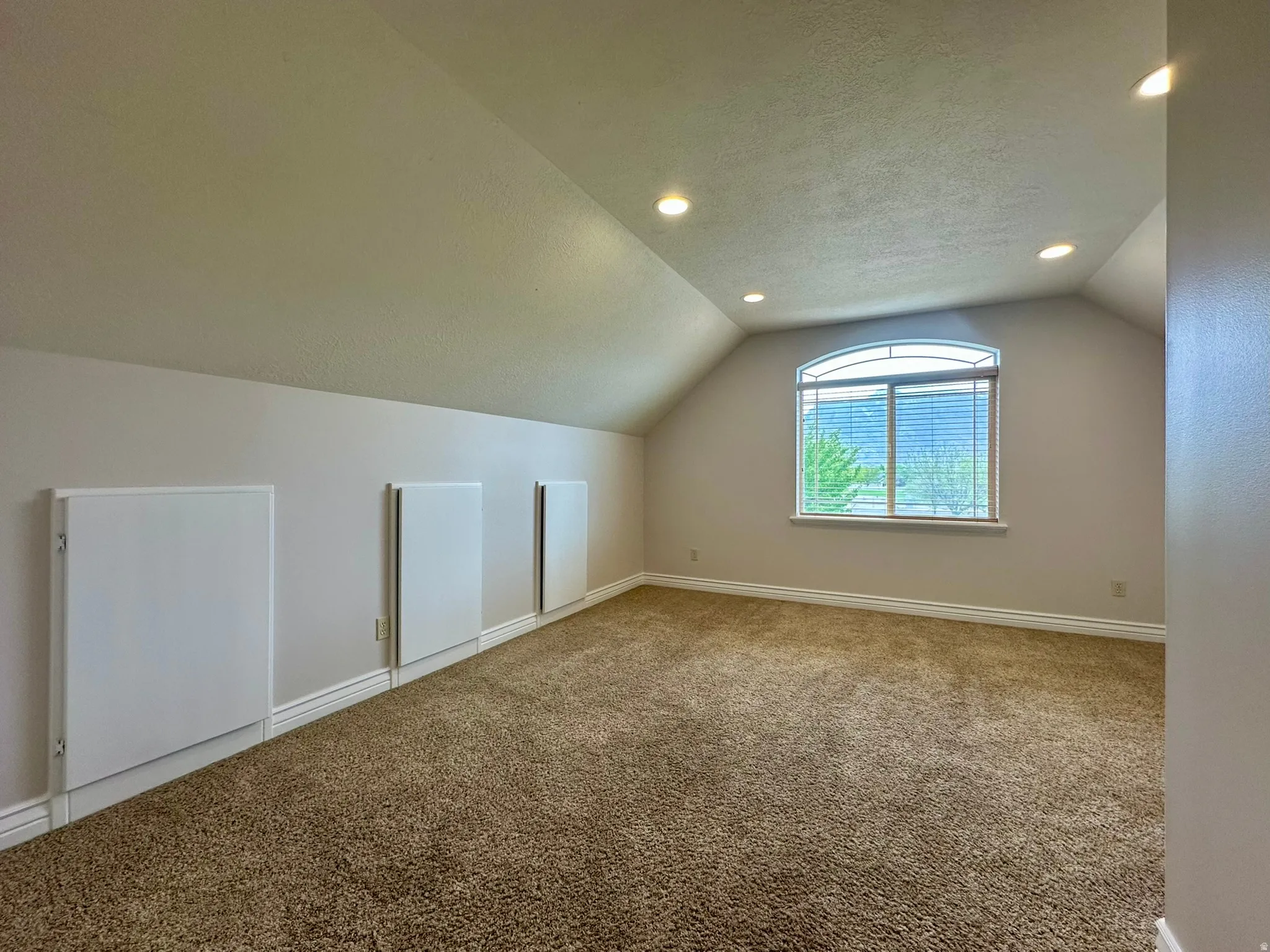 Bedroom featuring vaulted ceilings with recessed lighting, plush carpeting, and an arched window with blinds