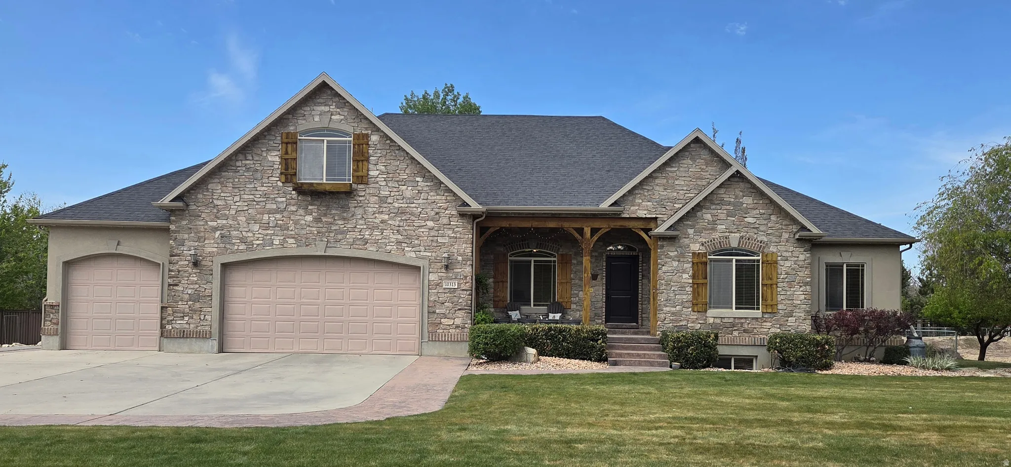 Craftsman-style home featuring a porch, concrete driveway, a front yard, and stone siding